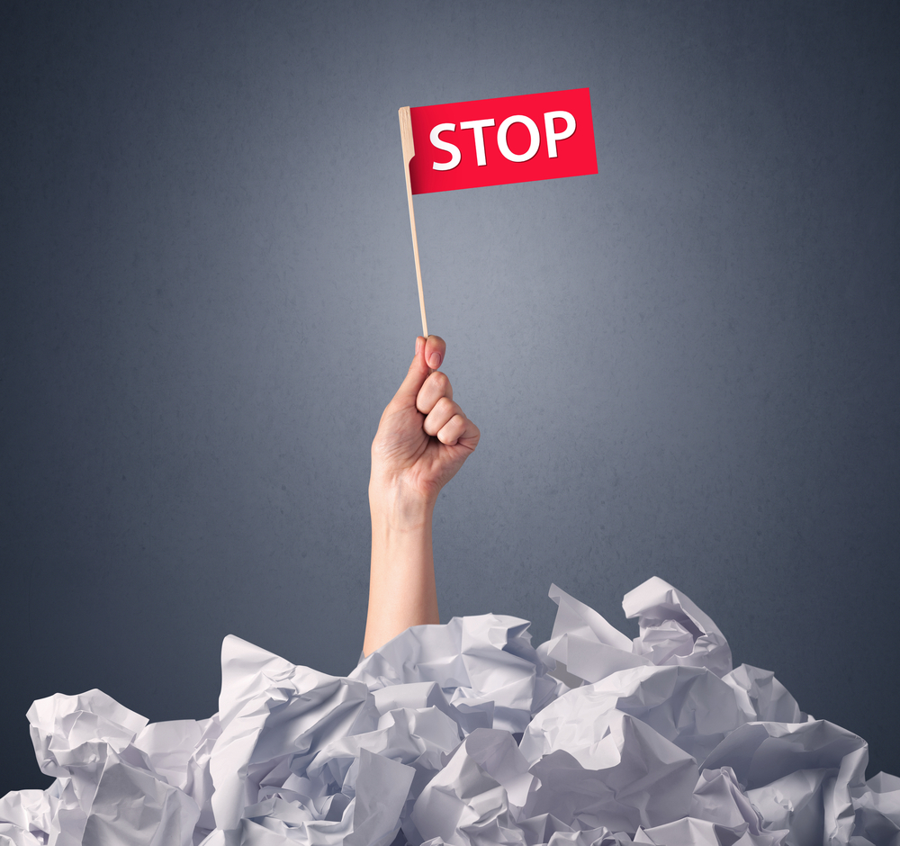 Female hand emerging from crumpled paper pile holding a red flag with stop written on it