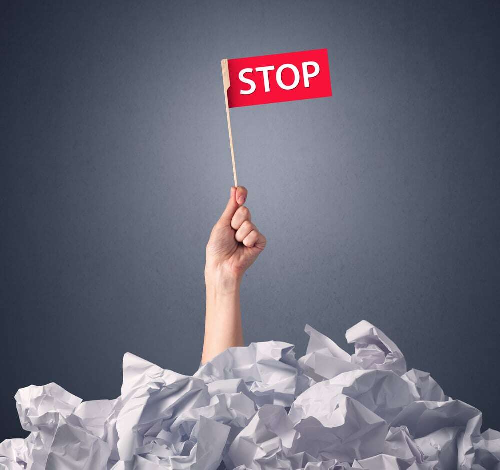 Female hand emerging from crumpled paper pile holding a red flag with stop written on it
